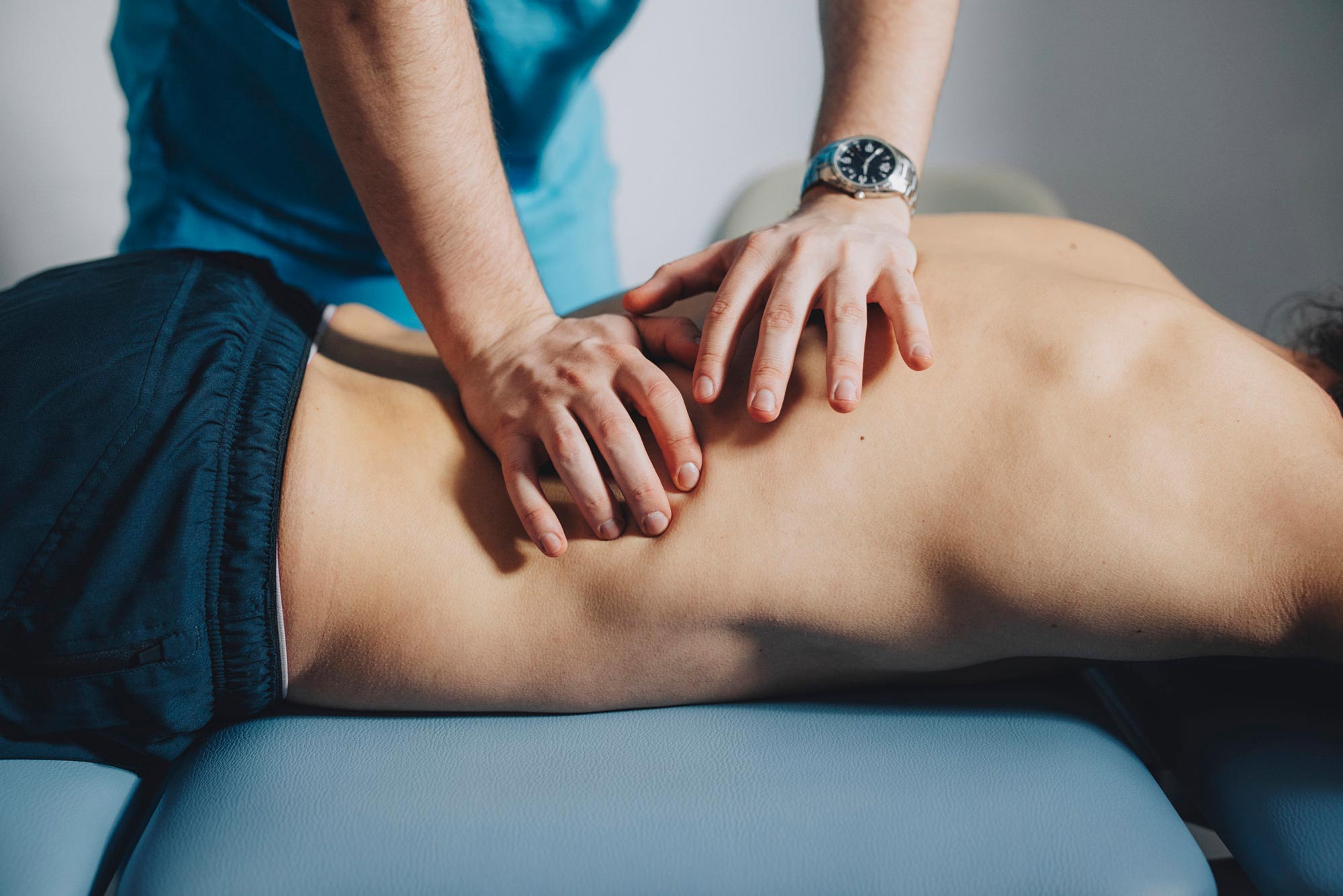 Sjukgymnast använder båda händerna för att massera ländryggen på en manlig patient som ligger på mage.