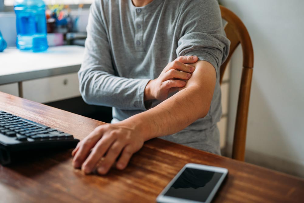 Man som känner smärta i armbågen när han sitter vid datorn